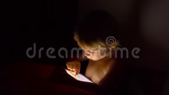 小男孩坐在黑暗的房间里玩平板电脑视频的预览图