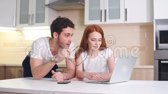 快乐的商务夫妇在厨房的家里看笔记本电脑视频的预览图