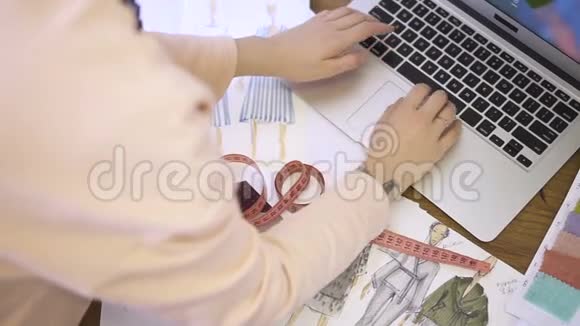 在笔记本电脑上工作的女裁缝手的俯视图视频的预览图