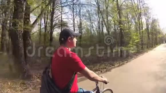 英俊的年轻人在夏天天骑自行车穿过阳光明媚的公园动作摄影机慢动作视频的预览图