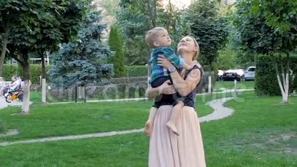 快乐的微笑妈妈拥抱着她在公园里蹒跚学步的儿子视频的预览图