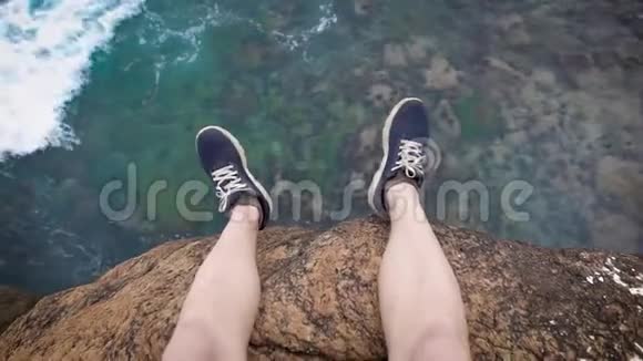 穿着深蓝色运动鞋的人的双腿悬在悬崖边的巨浪下面视频的预览图