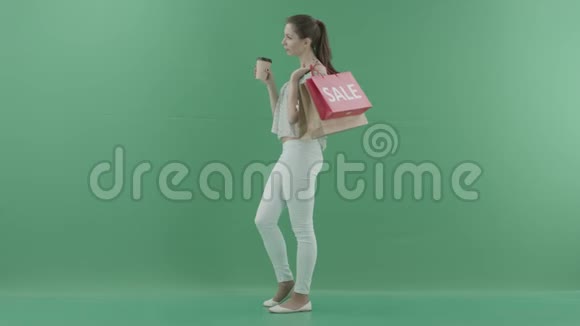 迷人的年轻女子喝着咖啡把袋子放在绿色的屏幕上视频的预览图