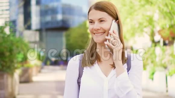 微笑的女商人穿着白色衬衫站在市中心的商业大厦里在智能手机上讲话视频的预览图