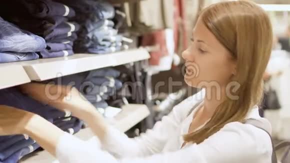 年轻女子在商场购物站在货架旁边衣服拿起牛仔裤感觉材料视频的预览图