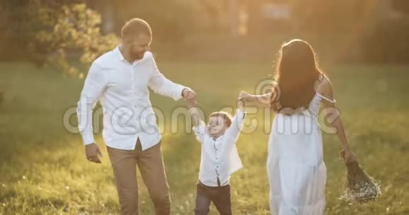 有宝宝的年轻幸福家庭日落时他们去了风景如画的绿野这个男孩是由父母抚养的日落视频的预览图