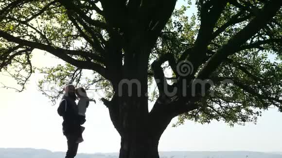 父亲牵着女儿的手在一棵大树旁说话视频的预览图