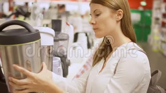 年轻女子在商店买厨房用具拿起热水瓶选择水壶视频的预览图
