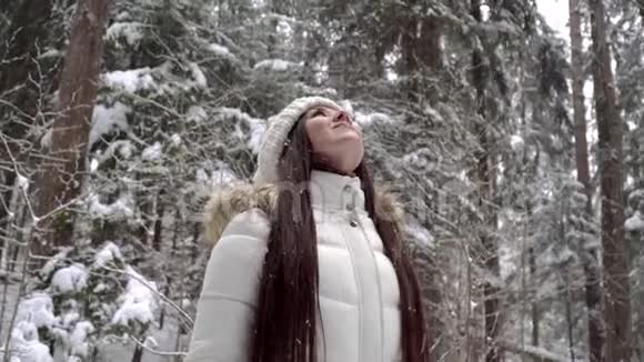 一个女孩正在冬天的森林里享受降雪一个美丽的女孩长着一头乌黑的长发穿着一件白色的夹克在冬天行走视频的预览图