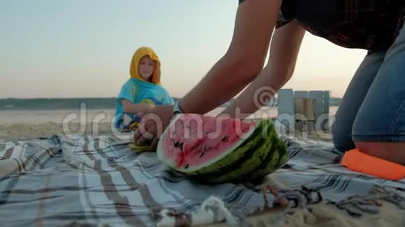 快乐的女孩在海滩上吃西瓜片父亲切西瓜夏天在户外野餐视频的预览图