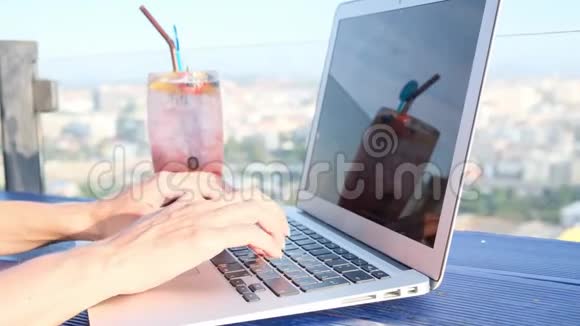 在一栋高楼屋顶的咖啡馆里一位女性在笔记本电脑上打字她可以看到城市的美丽全景视频的预览图