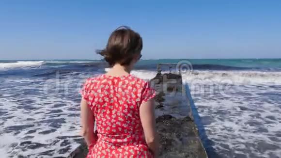 年轻迷人的白种人女人穿着红色的裙子走在码头上赤脚的双腿朝着码头上的大海走去视频的预览图