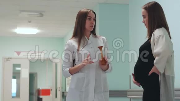 一位孕妇走在移植中心的走廊里与穿着白色晨衣的医生交流视频的预览图