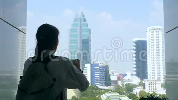 带背包的年轻少女正在智能手机上拍照看到曼谷城市的摩天大楼视频的预览图