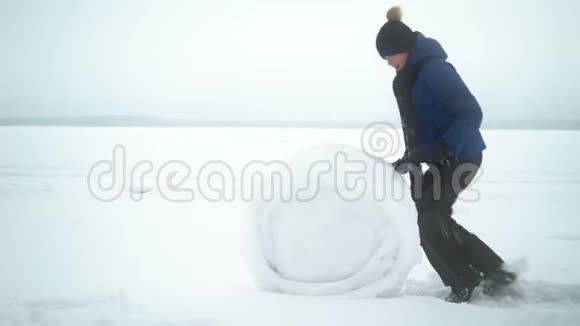 男孩在冬天为雪人滚动大雪球视频的预览图