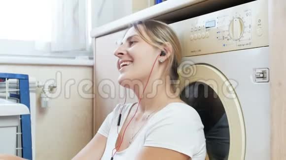 4k镜头快乐的年轻女子在洗衣服的时候用耳机听音乐视频的预览图