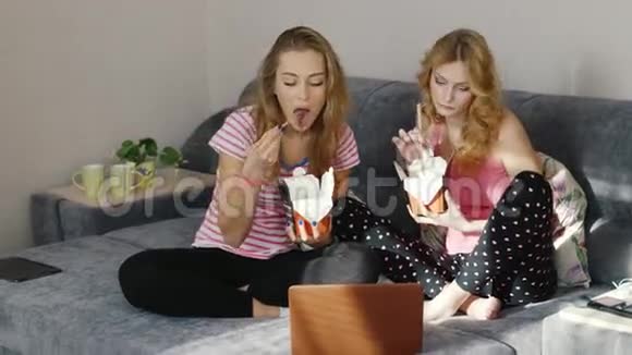 朋友们在家吃快餐在笔记本电脑上看电影帕贾马党两名年轻妇女视频的预览图