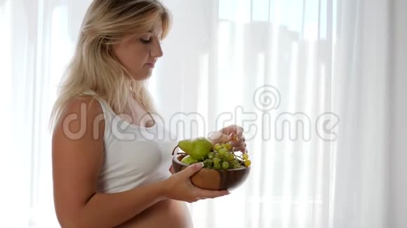 怀孕期间的饮食大肚子的女孩拿着装有水果的木盘吃葡萄视频的预览图