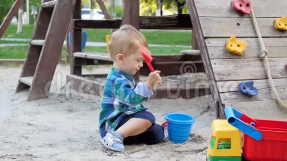 公园操场上可爱的幼儿男孩挖沙和倒塑料桶的慢动作视频视频的预览图