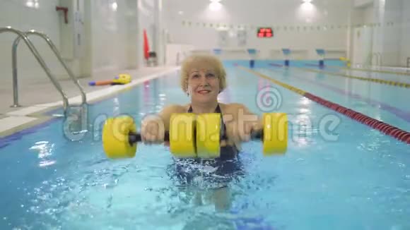 老妇人在游泳池里用哑铃训练双手视频的预览图