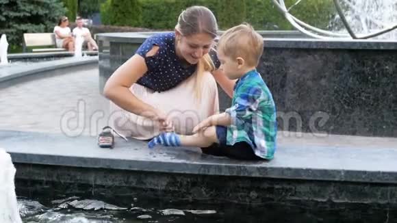 在公园的喷泉中玩耍后年轻母亲从蹒跚学步的儿子手里拿湿衣服的慢动作视频视频的预览图