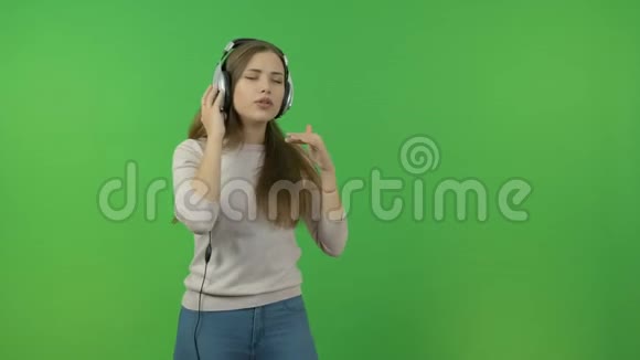 长头发的漂亮女孩通过耳机听音乐在绿色的屏幕上她跳舞唱歌视频的预览图