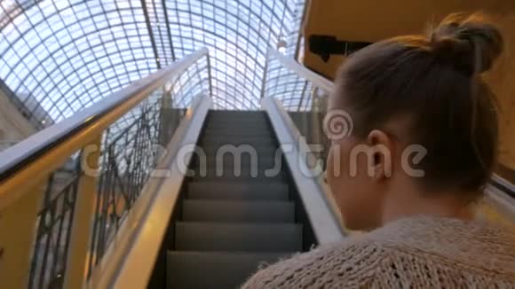 一位年轻女子在自动扶梯上走动在商场里四处张望视频的预览图