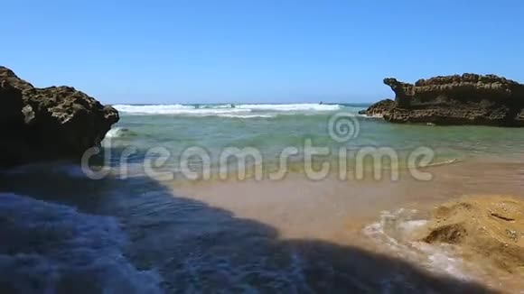 在两块岩石之间的小海湾里波涛汹涌的海洋在金色的海岸上翻滚视频的预览图