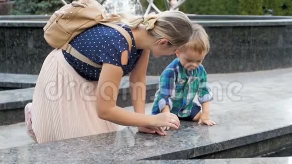 年轻母亲在公园里给她蹒跚学步的儿子展示喷泉的慢镜头视频的预览图