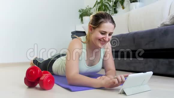 4k镜头年轻的运动女性躺在家里的健身垫和使用数字平板电脑视频的预览图