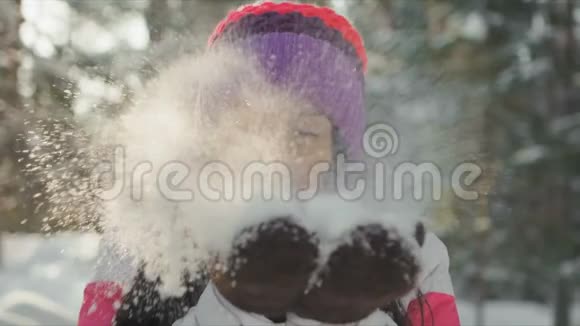 在冬天快乐美丽的年轻女子从她的手中吹出雪花视频的预览图