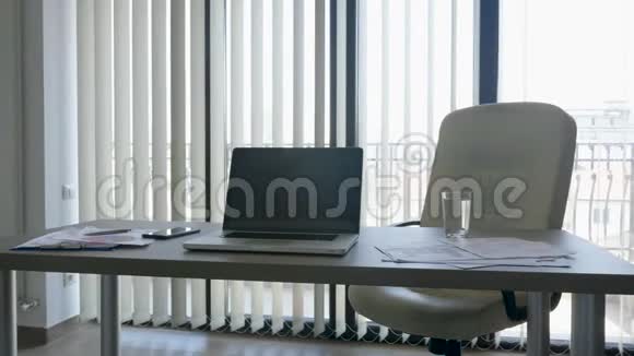 桌子上有笔记本电脑在现代化办公室的大窗户上视频的预览图