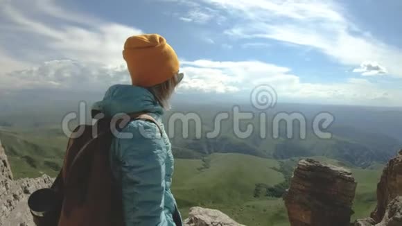 戴着帽子的金发女孩摄影师在她的数码相机上拍摄一张照片照片背景是高加索地区的岩石视频的预览图