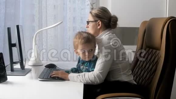 4k视频优雅的年轻女商人与她的孩子坐在办公室时通过电话和电脑聊天视频的预览图