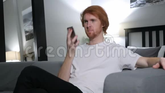 红头发的男人打电话坐在卧室的沙发上视频的预览图