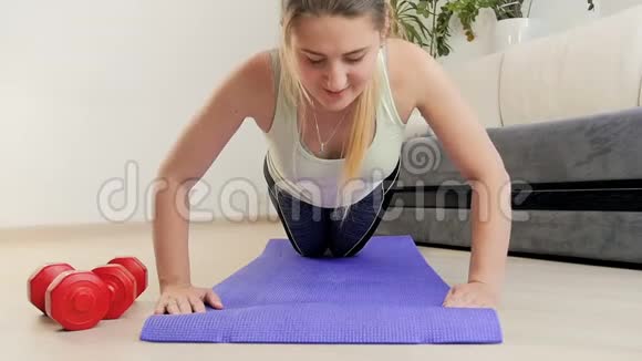 在家里的健身垫上做俯卧撑的漂亮年轻女人的慢动作镜头视频的预览图