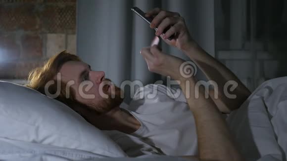 红发胡子男在床上浏览电子邮件和电话留言视频的预览图