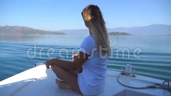 在阳光明媚的日子里年轻女子坐在船头眺望美丽的自然景观快乐的女孩视频的预览图
