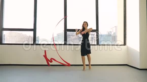 布鲁内特年轻女子舞蹈艺术体操现代用红色丝带穿黑色连衣裙在窗户前太阳视频的预览图