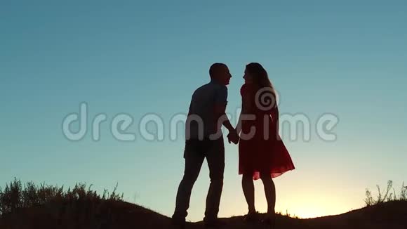 一对情侣剪影遛吻爱牵着手走向太阳在夕阳下戏剧性的天空背景和狗视频的预览图