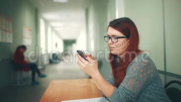 女大学生在大学学院的智能手机上看作业时做笔记坐着的女人视频的预览图