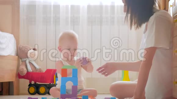 快乐的妈妈和宝宝在家里地毯上玩玩具侧面看一对快乐的母子玩玩具视频的预览图