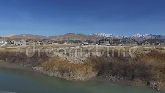 空中镜头从河岸开始然后飞越一片干草田飞向现代郊区的家园视频的预览图