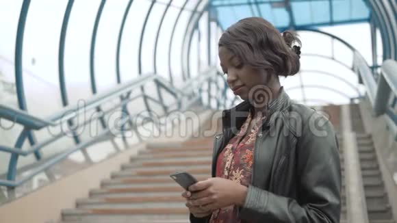 非裔美国女孩学生在街道城市街道地铁里用她的手机工作快乐地关门视频的预览图