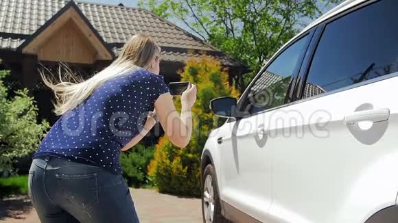 年轻女司机在智能手机上拍摄汽车销售照片的慢镜头视频的预览图