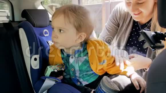 4k录像显示年轻母亲在孩子的汽车座椅上系安全带视频的预览图