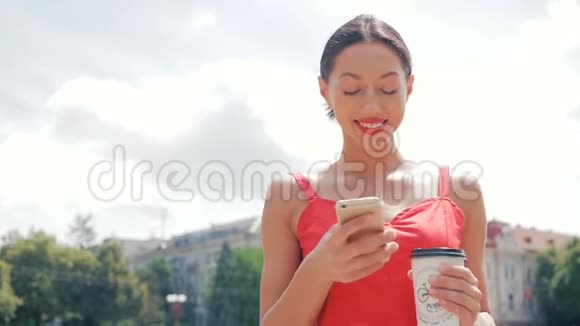 一位年轻美丽的时髦女人穿着红色的衣服在城市里走来走去喝着咖啡在电话里交谈视频的预览图