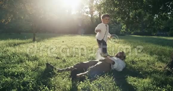 年轻的父亲和他的小儿子正在后院玩耍他们躺在草坪上视频的预览图