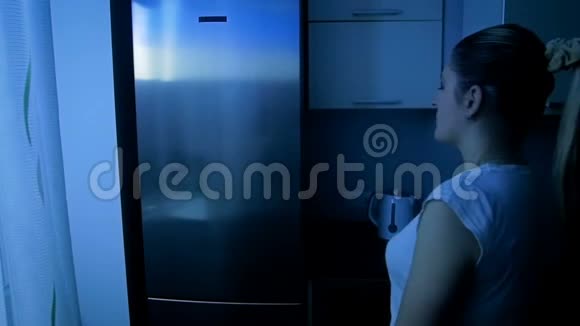 一个穿着睡衣从冰箱里拿食物的小睡女人的慢镜头视频的预览图