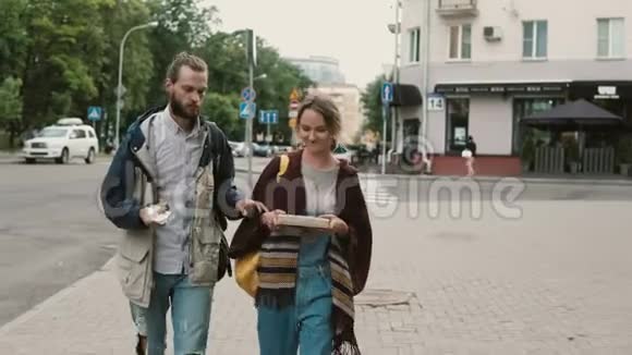 年轻漂亮的夫妇一起走在市中心男人吃快餐女人拿着礼物的盒子视频的预览图